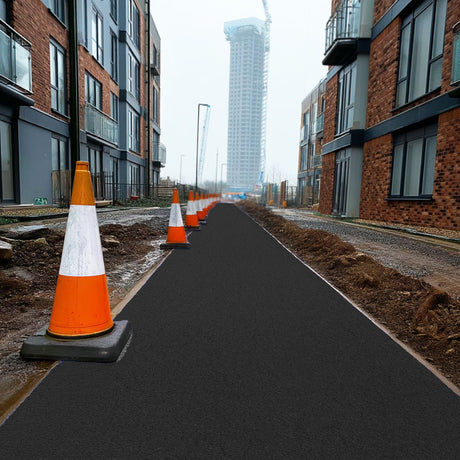 Row of orange traffic cones on a black walkway site mat with modern buildings in the background.