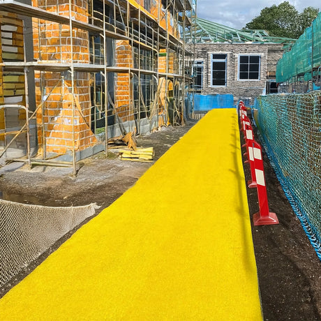 Construction site with a yellow walkway site mat, scaffolding, and building materials.