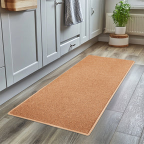 Beige rug on a wooden floor in a kitchen setting with cabinets and a plant.